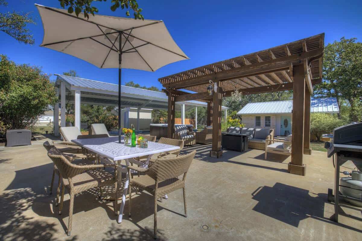 An outdoor patio with a table and chairs, a pergola, and a grill area.