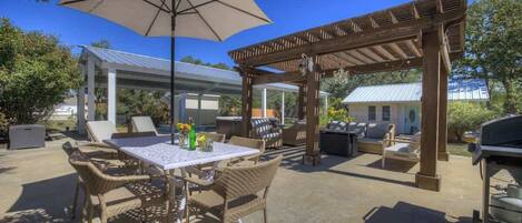 An outdoor patio with a table and chairs, a pergola, and a grill area.
