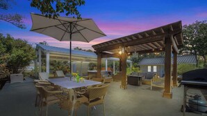 An outdoor patio with a pergola, dining table, and chairs. - Weitz Haven (Fredericksburg)