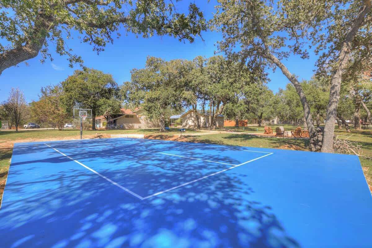 A blue outdoor basketball court surrounded by trees and houses.