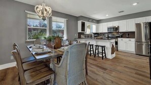 A modern kitchen with white cabinets, stainless steel appliances, and a dining area with wicker chairs and a chandelier. - Weitz Haven (Fredericksburg)