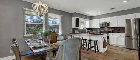 A modern kitchen with white cabinets, stainless steel appliances, and a dining area with wicker chairs and a chandelier.