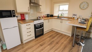 A compact kitchen with white cabinets, a black oven, a microwave, and a window. - Henhill Lodge (Chathill)