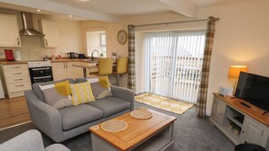 A modern living room with a grey sofa, a wooden coffee table, and a TV on a wooden stand. - Henhill Lodge (Chathill)