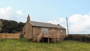 A stone house with a wooden deck and a small staircase leading to a door. - Henhill Lodge (Chathill)