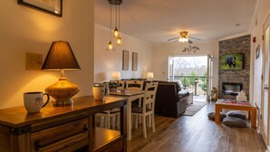 Una sala de estar acogedora con una mesa de centro de madera, una lámpara y una chimenea. Hay un comedor con una mesa y sillas, y una cocina al fondo.