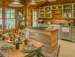 A wooden cabin interior with a dining area, kitchen, and built-in shelves.