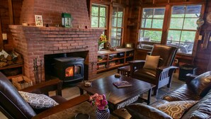 A cozy living room with a brick fireplace, leather furniture, and large windows. - Private Lakehouse with Great Swimming and Epic Sunset Views (Colchester)