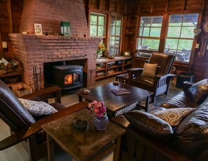 A cozy living room with a brick fireplace, leather furniture, and large windows.