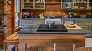 A wooden cabin interior with a central island, wooden cabinets, and a window. - Private Lakehouse with Great Swimming and Epic Sunset Views (Colchester)