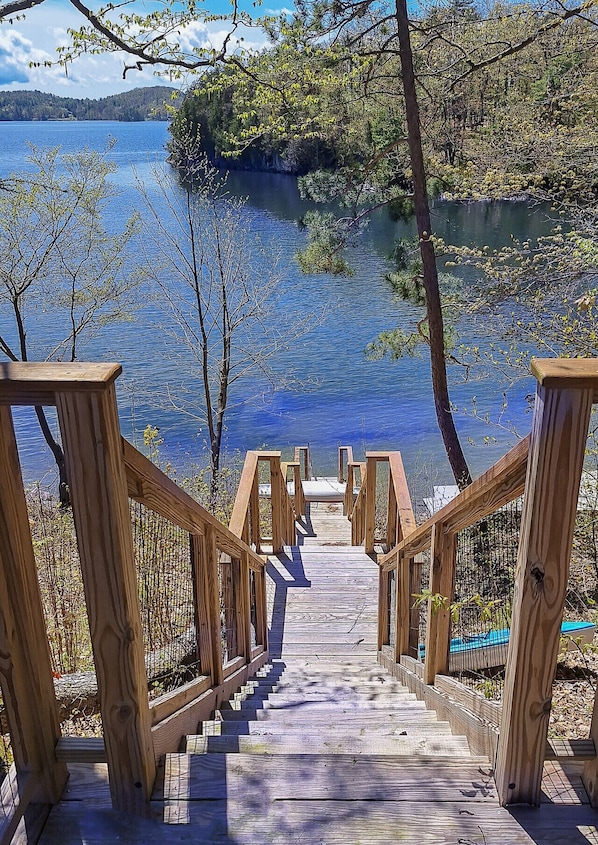 A wooden pathway leading to a dock over water, surrounded by trees and a clear sky.