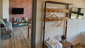 A room with a brick wall, a wooden bench with towels, a television, and a wooden rack with hangers. - CASAS RURALES MORADA DEL CERRO (Alcala del Jucar)