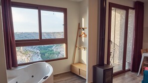 A modern bathroom with a large bathtub, a wooden bench, and a view of a cityscape through large windows. - CASAS RURALES MORADA DEL CERRO (Alcala del Jucar)