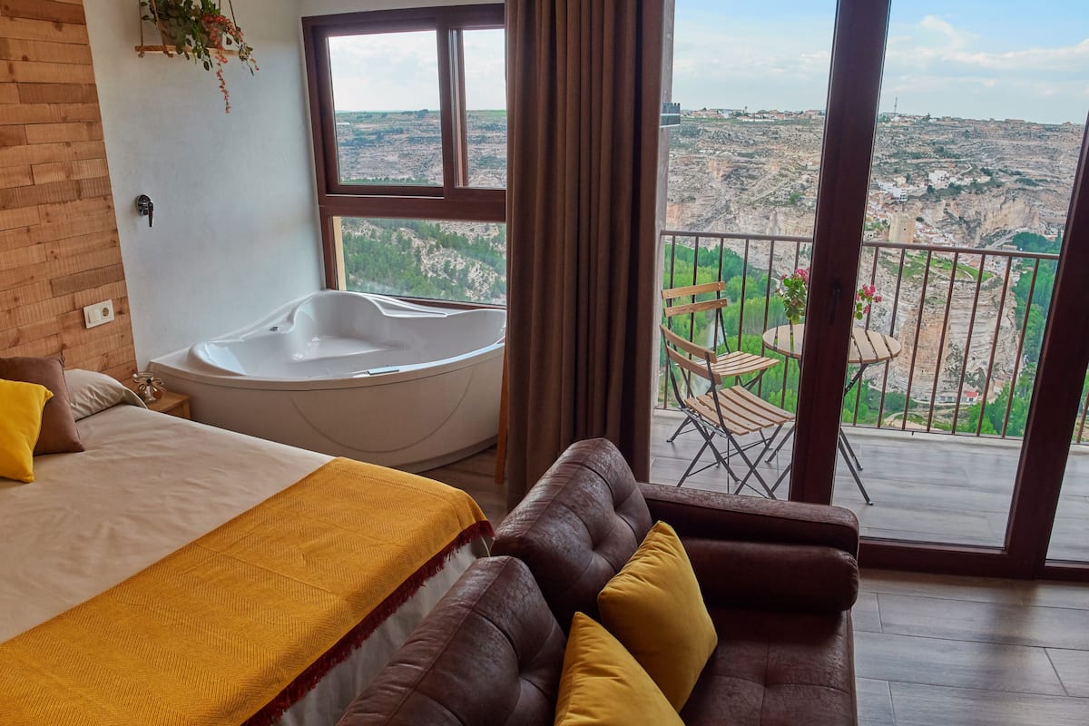 A bedroom with a large bed, a bathtub, and a balcony with a view.