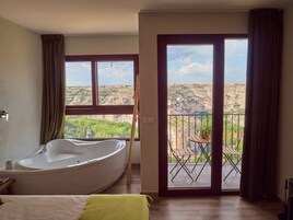 A bedroom with a large bathtub, a balcony with a table and chairs, and a view of a rocky landscape.