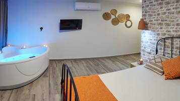 A modern room with a curved bathtub, a bed with orange bedding, a brick wall, and a mounted TV.