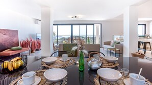 A modern dining area with a large table set for four, surrounded by wicker placemats and a green vase centerpiece. - Spacious villa w/ exceptional sea-view, pool & petanque ground _ 5 mn from beach (Lumio)