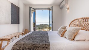 A bedroom with a bed, a wooden bench, a large window, and a view of the outdoors. - Spacious villa w/ exceptional sea-view, pool & petanque ground _ 5 mn from beach (Lumio)