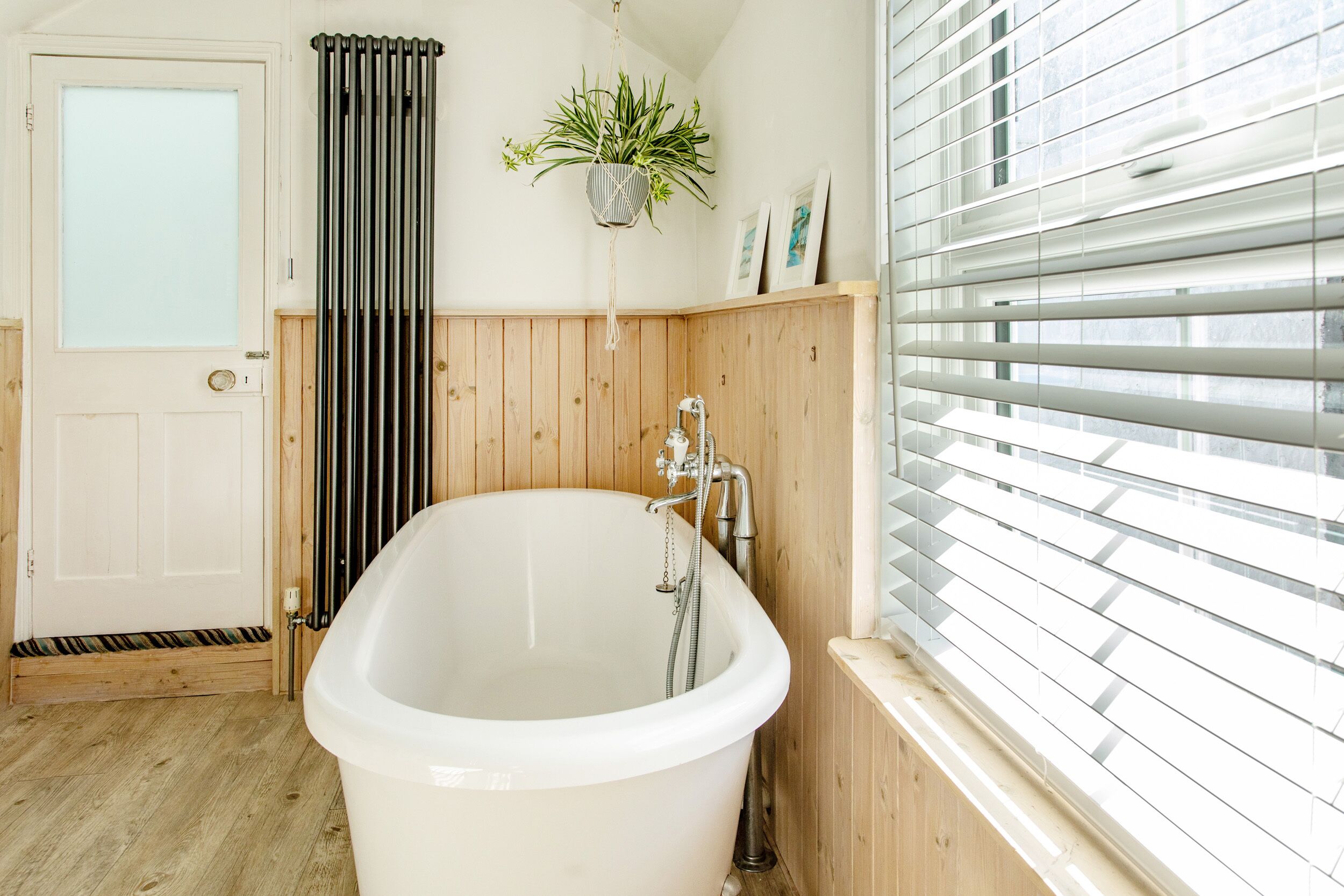 Un baño con una bañera independiente, paneles de madera, un radiador y una ventana con persianas.