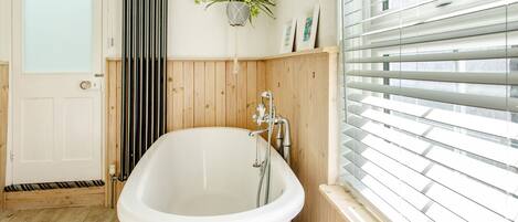 A bathroom with a freestanding bathtub, wooden paneling, a radiator, and a window with blinds.