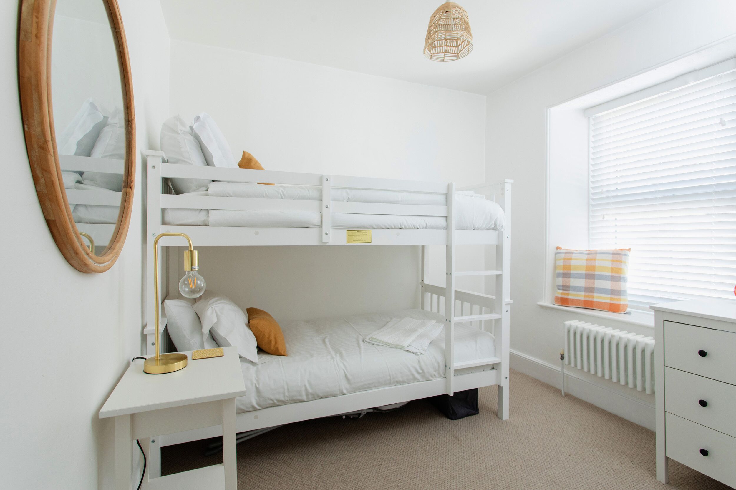 Un lit superposé avec un bureau et une chaise, un miroir et une fenêtre avec des stores.