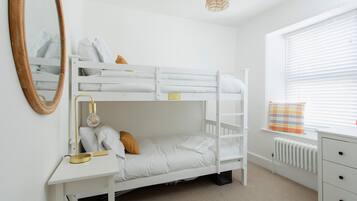A bunk bed with a desk and chair, a mirror, and a window with blinds.