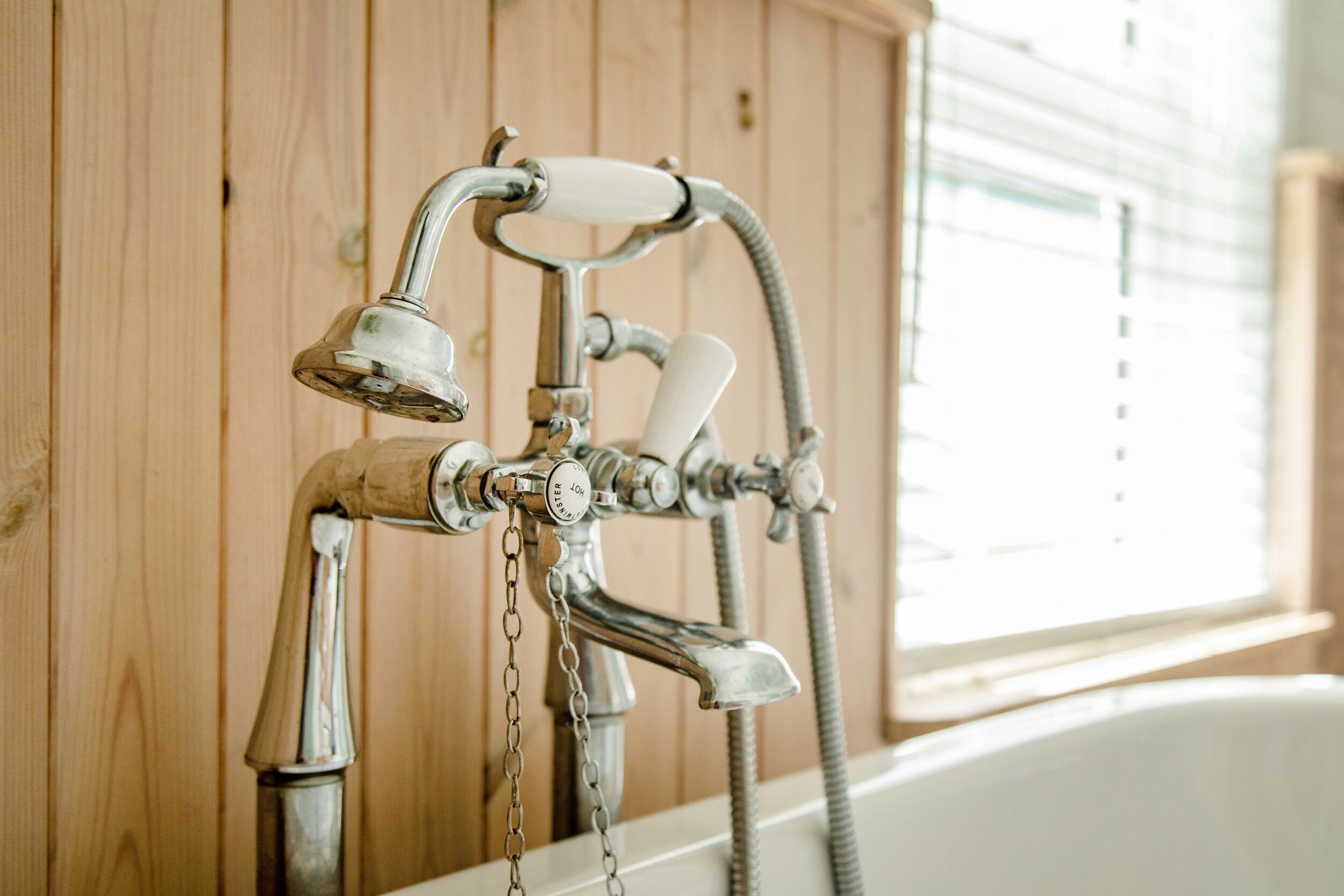A bathroom with a wooden wall, a bathtub, and a shower with a hose.