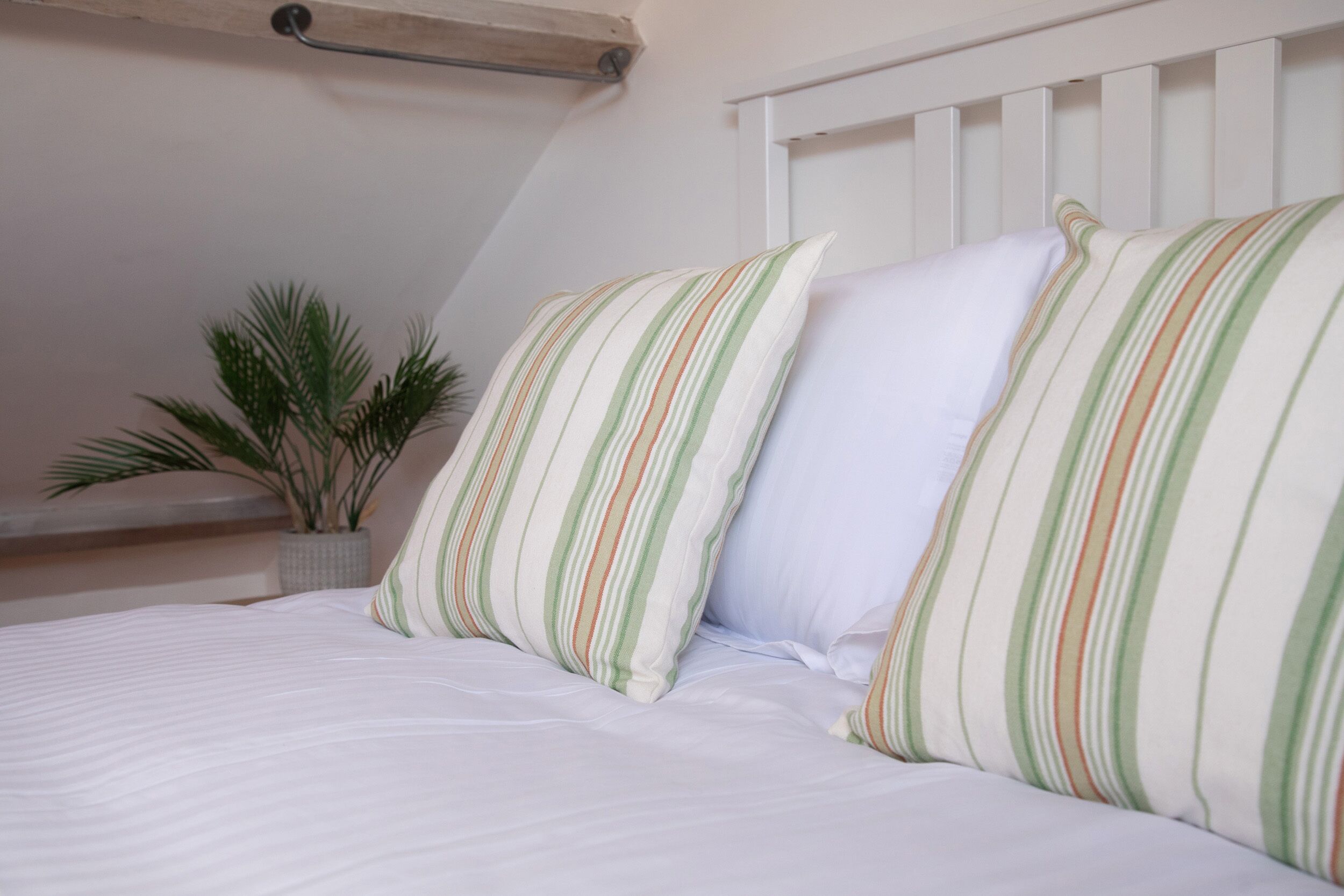 A neatly made bed with striped pillows and a potted plant.