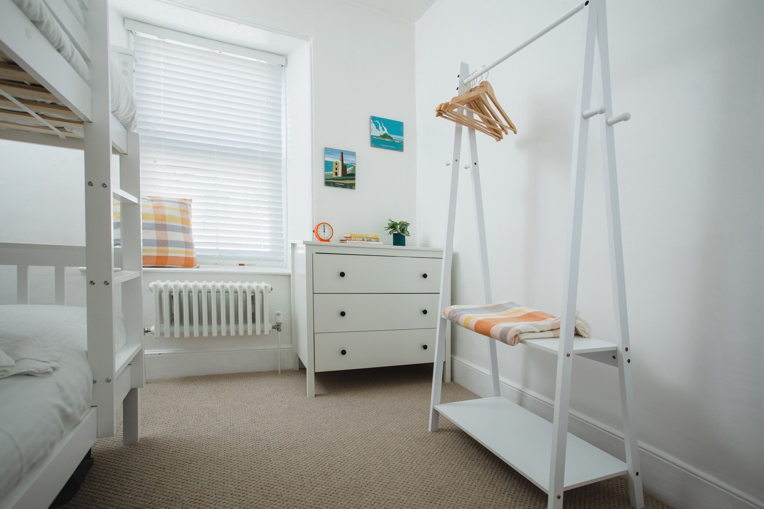 Habitación infantil con literas, cómoda, radiador y ventana con persianas.