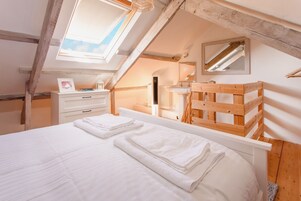 A bedroom with a skylight, wooden beams, a bed with white linens, a bedside table, and a mirror.