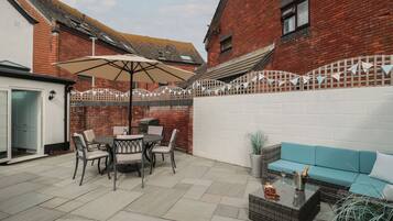 A patio with a table and chairs, a blue sofa, and a brick wall.
