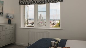 A bedroom with a large window overlooking a marina, a dresser, a radiator, and a bed with a blue cover. - Quay Cottage - Sea View (Poole)