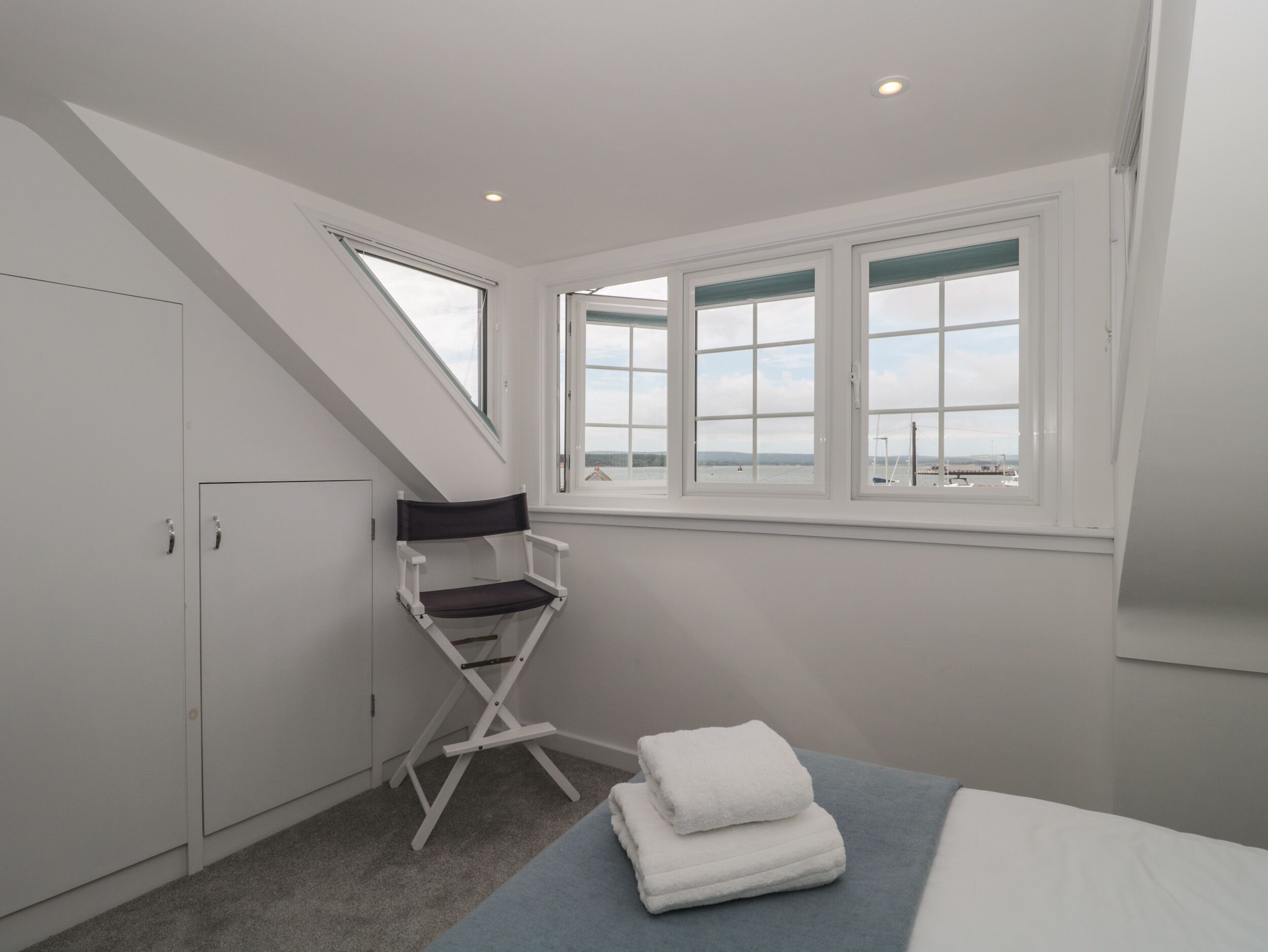 Un dormitorio con tragaluz, una cama, una silla y vista al mar.