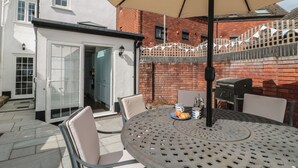 A patio with a round table, chairs, and a large umbrella. - Quay Cottage - Sea View (Poole)