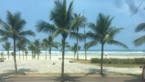 A beach with palm trees and a paved walkway. - Foot in the sand at Caiçara beach II (Praia Grande)