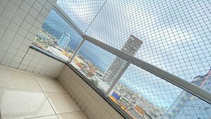 A room with tiled floors and a view through a mesh window to a cityscape with buildings. - Foot in the sand at Caiçara beach II (Praia Grande)