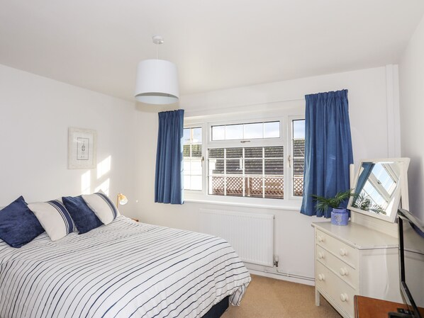 A bedroom with a bed, a dresser, a window with curtains, a radiator, and a hanging light fixture. - Neaudd Wen (Pentraeth)