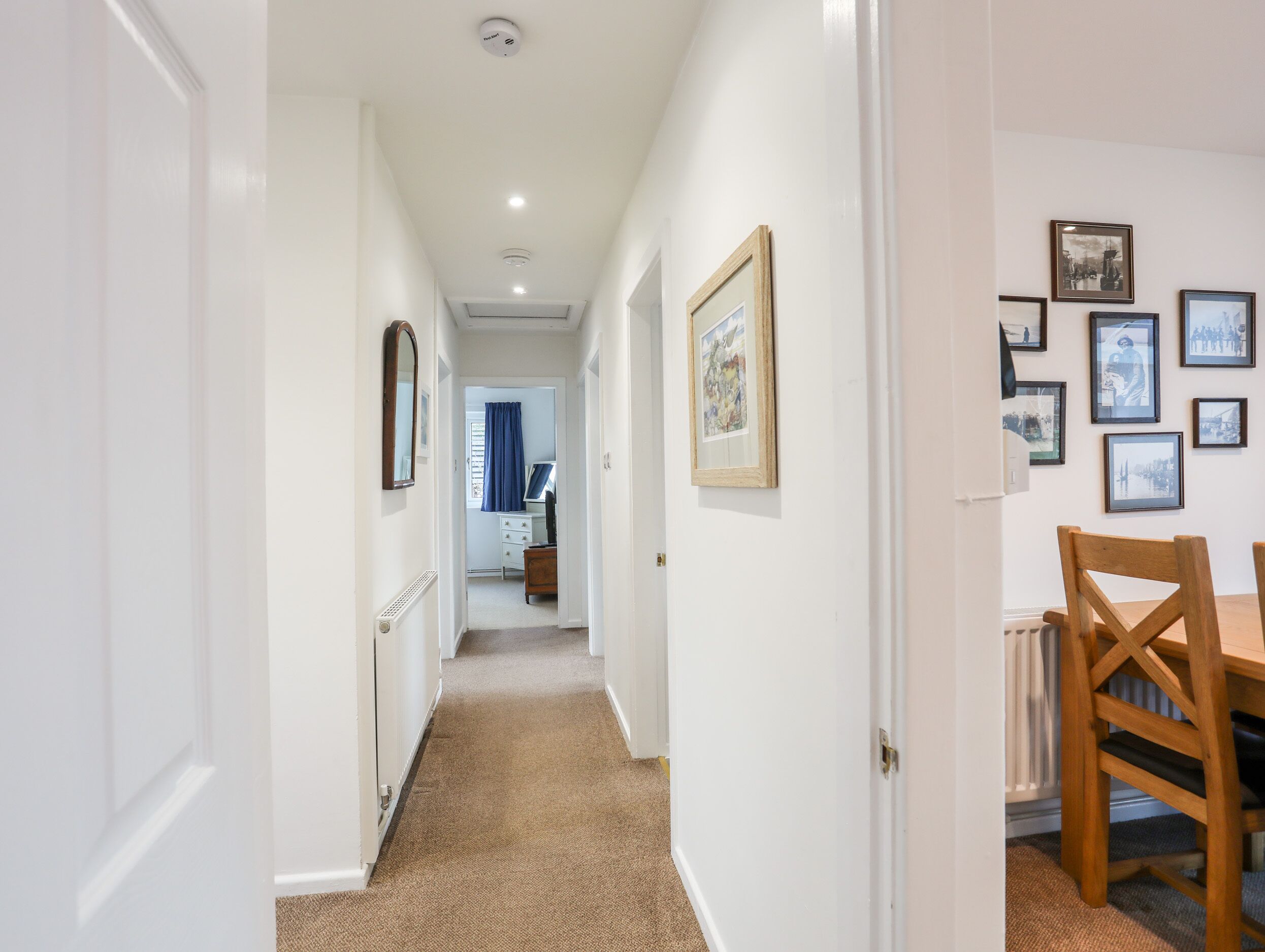 A hallway with white walls, a wooden chair, and framed pictures on the wall.