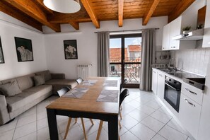Een moderne keuken met een eethoek, voorzien van een houten plafond, witte kasten en een groot raam met gordijnen.