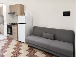 A kitchenette with a stove, oven, and refrigerator, a grey sofa, and a patterned rug. - BIG Suite Goldoni [Duomo-M4 Lin Airport] (Milan)