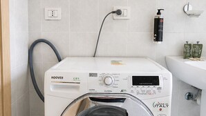 Een wit wasmachine met voorlader, een bedieningspaneel, een stopcontact en een wandbevestigde zeepdispenser.