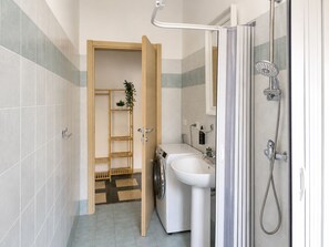 Une petite salle de bain comprenant une douche, un lavabo et un lave-linge.