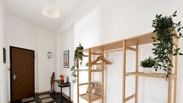 Een gang met een zwart-wit geruite vloer, een houten schapkas met planten, en een deur.