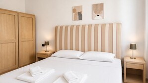 A hotel room with a large bed, wooden wardrobe, two bedside tables with lamps, and artwork on the wall.