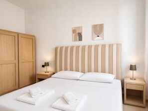 Une chambre d’hôtel avec un grand lit, une armoire en bois, deux tables de chevet avec des lampes et des œuvres d’art accrochées au mur.