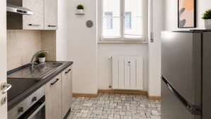 A modern kitchen with a stainless steel refrigerator, a built-in oven, a sink, and a window with blinds.
