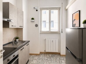Une cuisine moderne équipée d’un réfrigérateur en acier inoxydable, d’un four encastré, d’un évier et d’une fenêtre avec des stores.