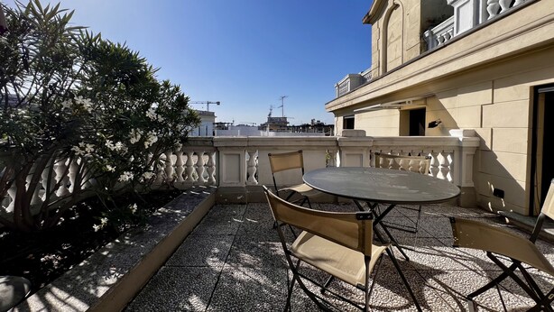 Eine Dachterrasse mit einem runden Tisch und zwei Stühlen, umgeben von einer verzierten Brüstung und Topfpflanzen.