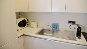 Una cocina con armarios blancos, microondas, tostadora, pileta y cafetera.