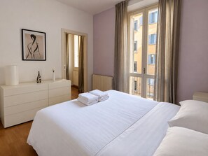 A hotel room with a bed, a dresser, a framed artwork, and a window with curtains.
